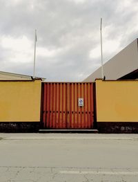 Gate and wall by road against sky