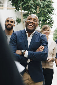 Happy mature colleague with arms crossed listening to entrepreneur outside office