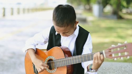 Close-up of boy playing guitar while standing at park