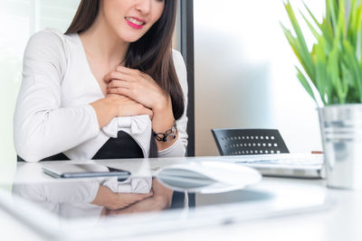 Midsection of woman using mobile phone while sitting on table