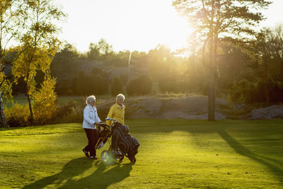 Senior women walking with golf bags on grassy area