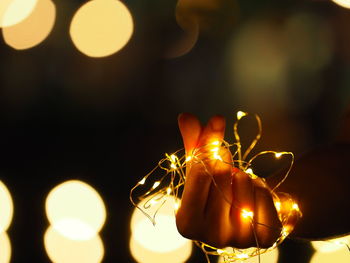 Close-up of hand amidst illuminated christmas lights