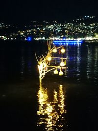 Illuminated city by river against sky at night