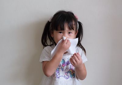 Cute girl holding tissue while standing against wall