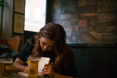 Young woman drinking glass while sitting on table