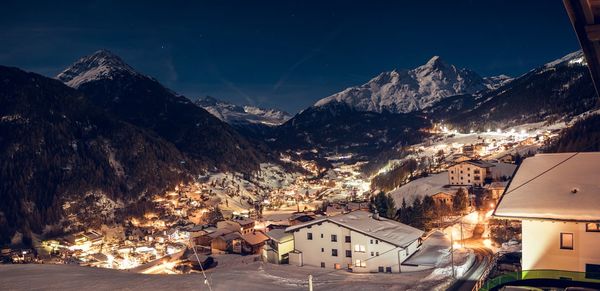 Illuminated houses by snowcapped mountains against sky at night