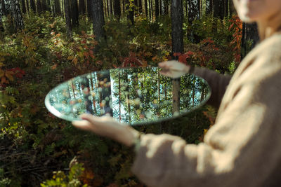 Midsection of woman holding mirror in forest