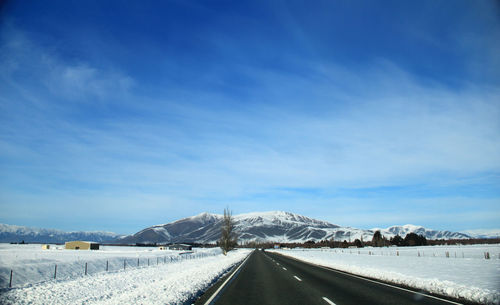 Road by snowcapped mountain against blue sky
