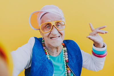 Portrait of happy senior woman gesturing against yellow background