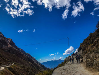 People walking on mountain against blue sky