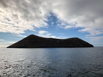 Scenic view of sea by mountain against sky