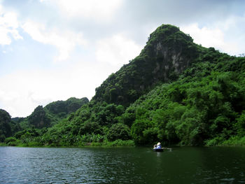 Scenic view of river by tree mountains against sky