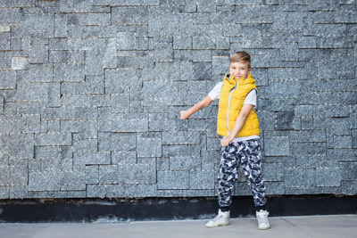 Full length portrait of boy dancing against stone wall