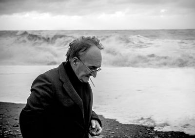 Side view of senior man smoking cigarette at beach