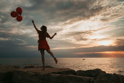 Full length of woman standing on rock at beach during sunset