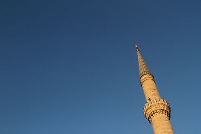 Low angle view of mosque minaret against clear blue sky