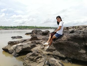 Woman sitting on rock by sea against sky