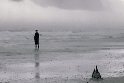 Silhouette man walking on beach against sky