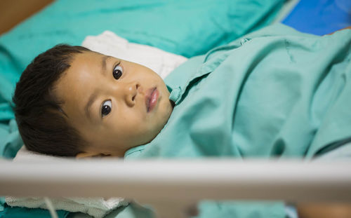 High angle portrait of cute boy lying on bed in hospital