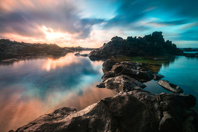 Scenic view of rocks in lake against dramatic sky during sunset