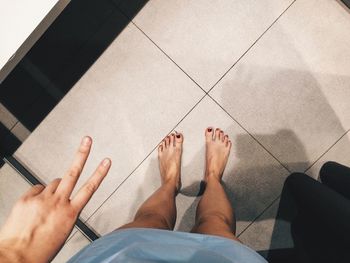 Low section of woman showing peace sign while standing on floor