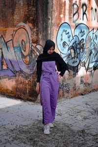 Full length of young woman standing against graffiti wall