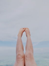 Low section of person legs by sea against sky