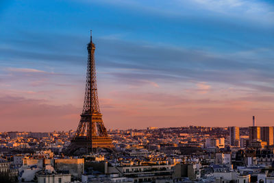 Communications tower in city against sky during sunset