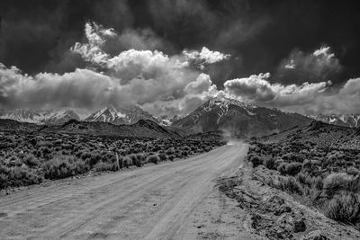 Panoramic view of dirt road leading towards mountains against sky