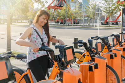 A hispanic woman taking a bicycle in a bike rental platform