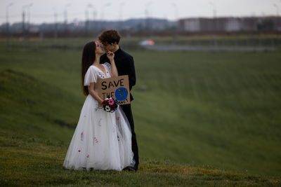 Beautiful newlyweds are kissing while holding a sign that says save the world