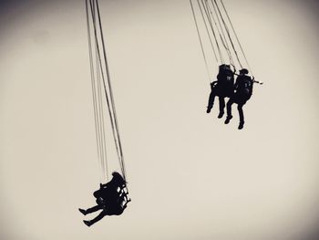 Low angle view of silhouette men paragliding against clear sky