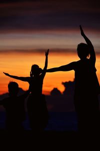 Silhouette people standing by sea against sky during sunset