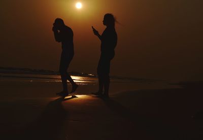 Silhouette people standing on beach against sky during sunset