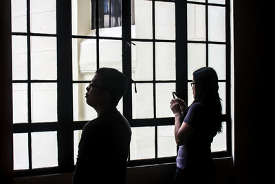 Man looking by woman using phone in front of building window