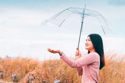 Side view of woman holding umbrella while standing on land against sky