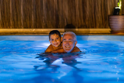 Grandfather and grandson playing in a swimming pool at night
