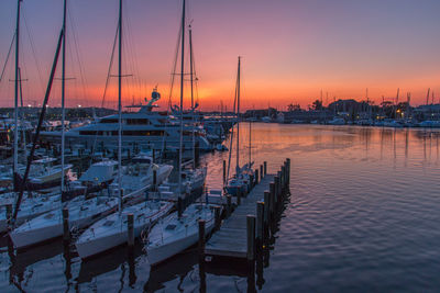 Sailboats moored in harbor at sunset