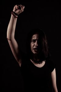 Portrait of young woman with arm raised standing against black background