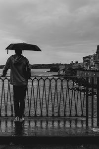 Rear view of man standing by railing against river during rainy season