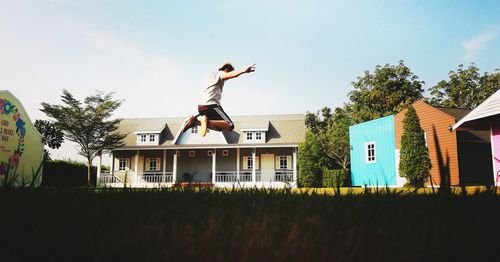 Man jumping outside house against sky