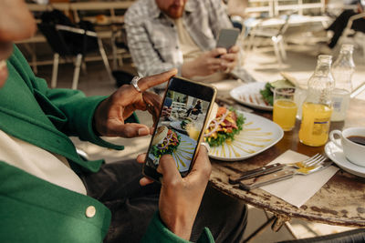 Man photographing food on table through smart phone at sidewalk cafe