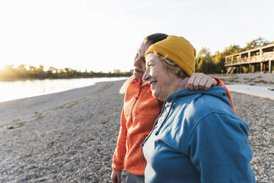 Fit grandmother and granddaughter walking at the river with arms around, having fun