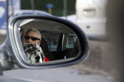 Man with dog reflecting in side-view mirror of car