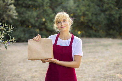 Woman in an apron hold a paper bag with eco products. delivery of organic bio products from farm. 