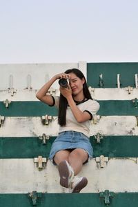 Full length of young woman photographing against clear sky