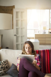 Girl using tablet computer while sitting on sofa at home