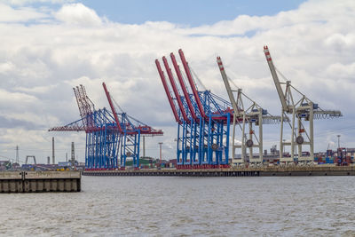 Cranes at commercial dock against sky