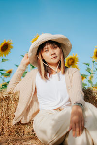 Young woman looking away while sitting on land against sky