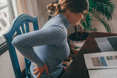 Side view of woman using digital tablet while sitting on sofa at home